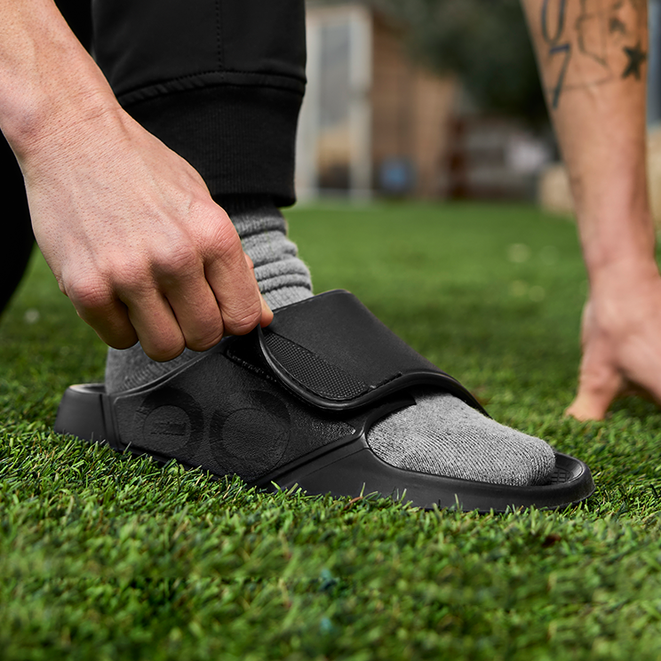 OOFOS OOahh Sport Flex Slide — Matte Black, adjusting the strap