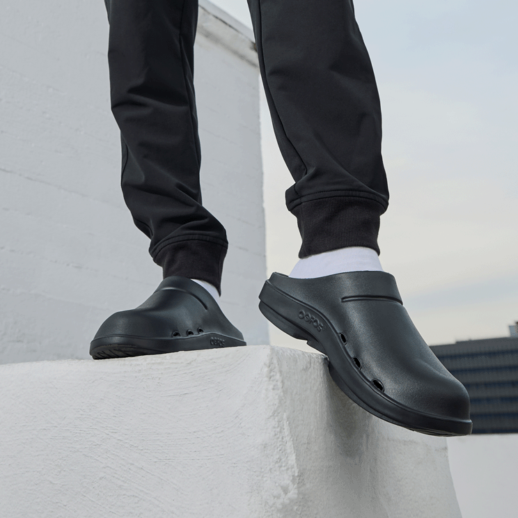OOFOS OOcloog Clog — Black, worn standing outside